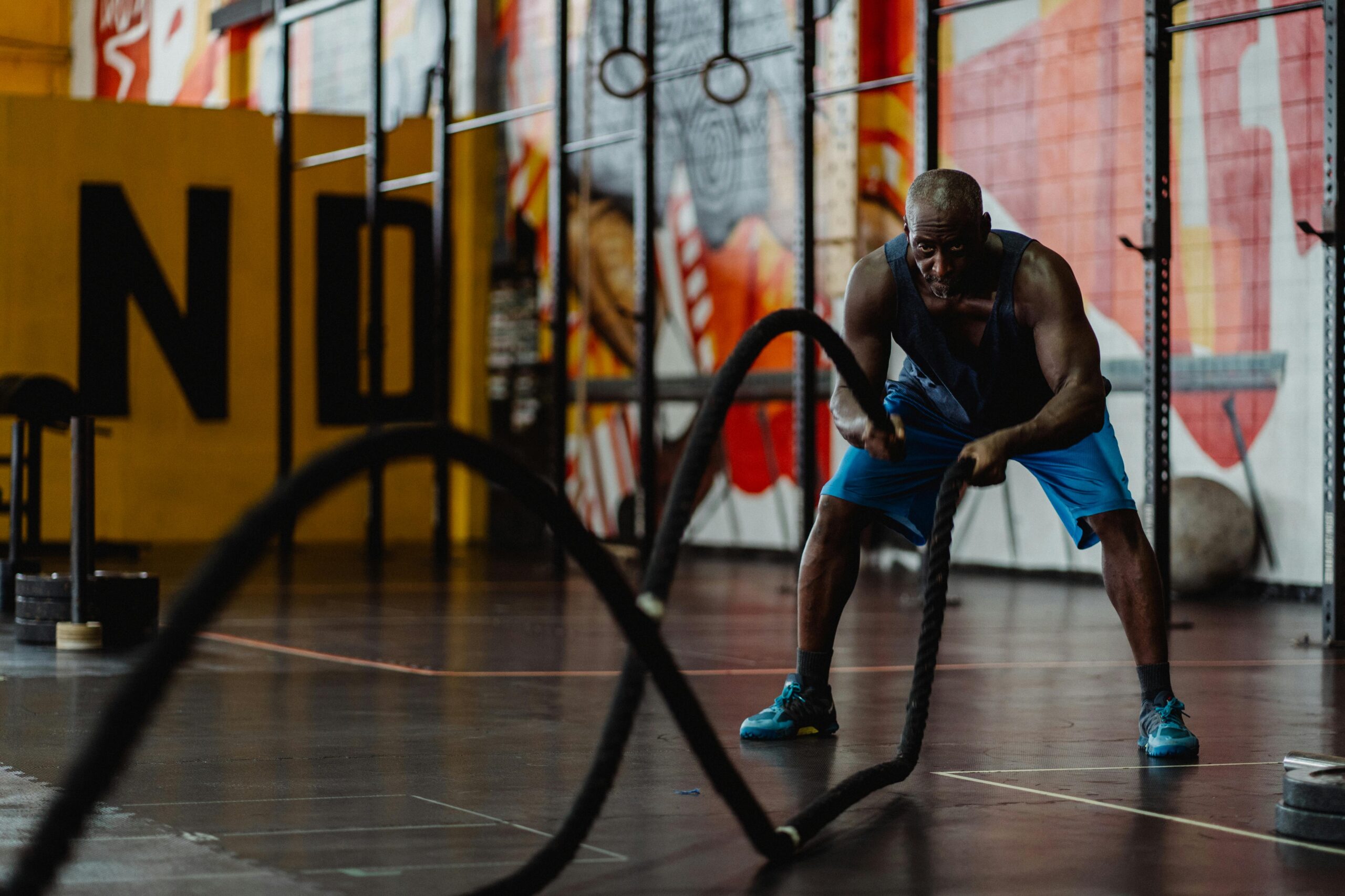A muscular man intensely exercises with battle ropes in an indoor gym setting, showcasing strength and fitness.